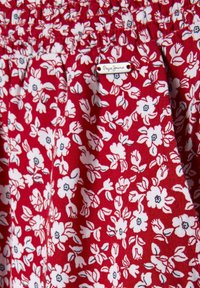 Czerwony materiał z kwiatowym wzorem w bieli i niebieskim, z elastycznym pasem i metką z napisem "Papa Jeans."