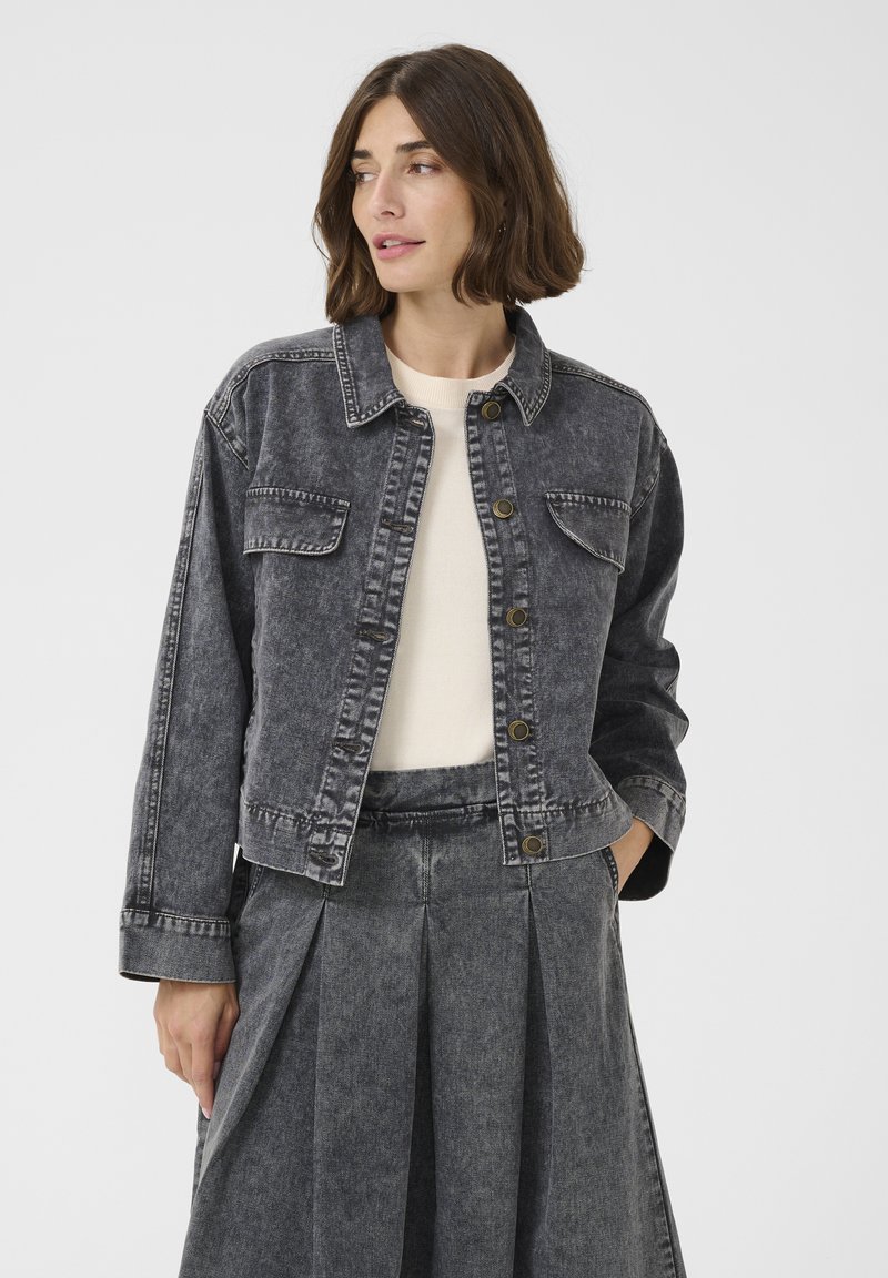 Denimjacka med en urtvättad svart nyans, knapfront, två bröstfickor och en cropped siluett. Materialet verkar vara texturerat och något nött.