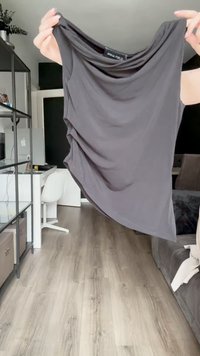 Top sem mangas cinza escuro com decote drapeado, textura suave, tecido leve e uma bainha ligeiramente assimétrica. Etiqueta da marca visível.