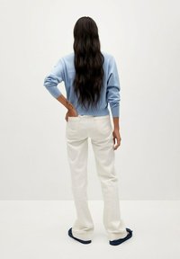 Jersey azul claro de manga larga, combinado con pantalones anchos blancos y sandalias azul oscuro, visto desde atrás.