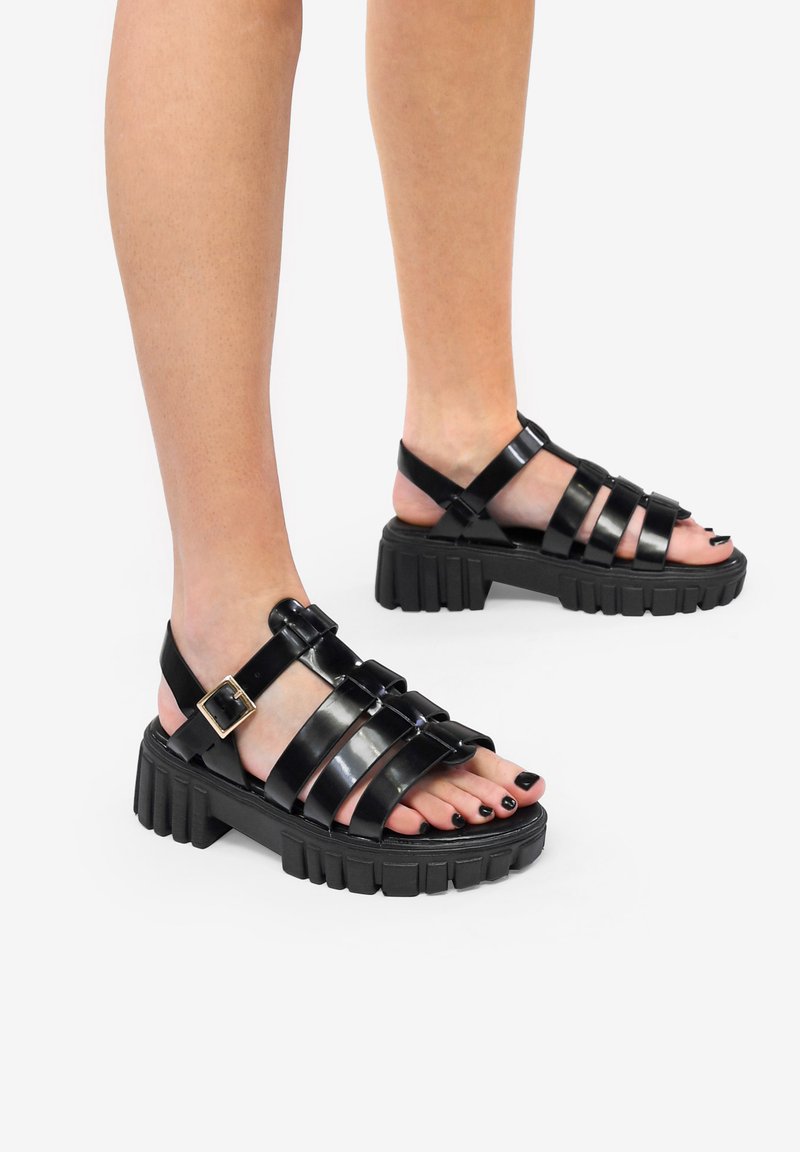 Sandali neri con cinturini e suola in gomma spessa, caratterizzati da materiale lucido, fibbia regolabile e design con punta aperta.