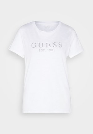 White cotton t-shirt with short sleeves, round neck, featuring "GUESS" and "EST. 1981" in rhinestones across the front. Soft texture, casual design.