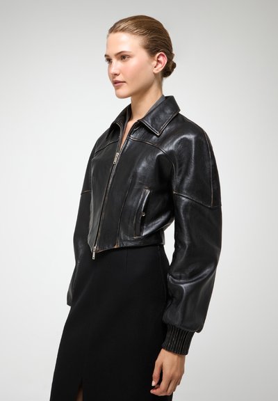 Chaqueta corta de cuero negro con cremallera frontal, gran cuello y mangas abullonadas. Incluye bolsillos laterales y puños acanalados.