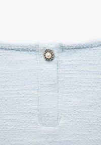 Helles blaues strukturiertes Gewebe mit einem zentralen Knopf, der eine Perle zeigt, umringt von kleinen klaren Kristallen, entworfen für den Verschluss.