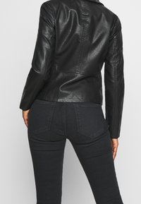 Giacca in pelle nera con design aderente e cuciture sulle spalle. Caratterizzata da una texture liscia, maniche lunghe e spacchi posteriori. Abbinata a jeans scuri.