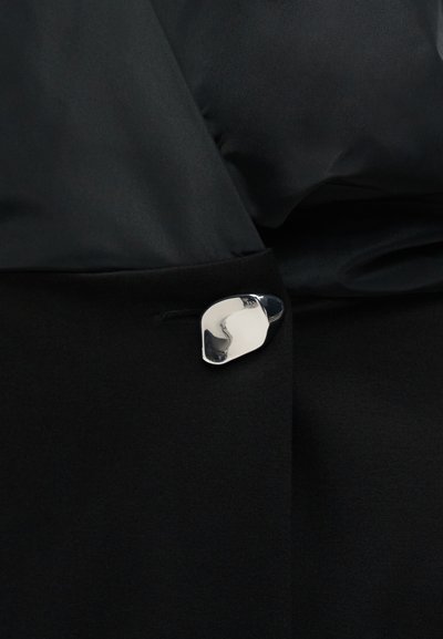 Tissu noir avec une fermeture en forme irrégulière argentée et brillante, fixant deux sections superposées.