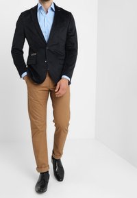 Marinblå kavaj med slät yta, bruna byxor, ljusblå skjorta och svarta skor; med en enkel knappstängning och bröstficka.