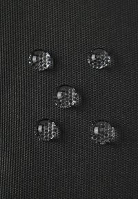 Fünf klare Wassertropfen, die auf einem schwarzen strukturierten Stoff ruhen und die wasserabweisenden Oberflächeneigenschaften hervorheben.