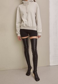 Světle šedá mikina s kapucí, v kombinaci s černými kraťasy a lesklými černými vysokými botami po stehna s krémovým blokovým podpatkem. Hladké textury po celé ploše.