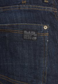 Mørkeblå denimjeans med gule sømmer, et merke merket "BLEND BUILT BLUE," og en glatt tekstur med et klassisk design.