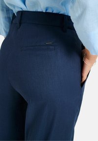 Námořnické modré lněné kalhoty s hladkou texturou, které mají zadní kapsu s malým černým akcentem a přiléhavým pasem.