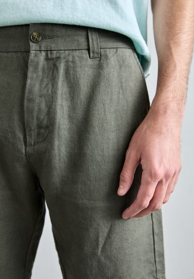 Pantalons en lin vert olive avec une fermeture à bouton, dotés d'une coupe décontractée, d'un tissu texturé et de légères variations de couleur naturelle.