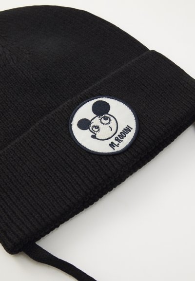 Svart strikket beanie med en rund hvit lapp som har et tegneserieansikt, svarte ører og teksten "M. ROONI." Teksturert stoff, tett passform.