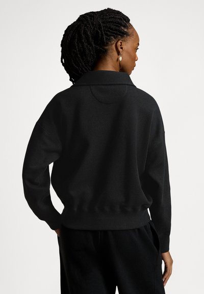 Juoda puloverio tipo sportinė palaidinė su sulankstomu apykakliu, ilgomis rankovėmis ir laisvo stiliaus siluetu. Minkšta, tekstūruota medžiaga su ribine apačia.