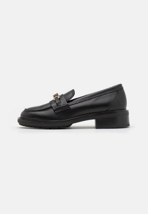 Mocassin noir en cuir avec petit talon, bout arrondi et détail boucle dorée à l'avant, présenté de profil sur un fond blanc.