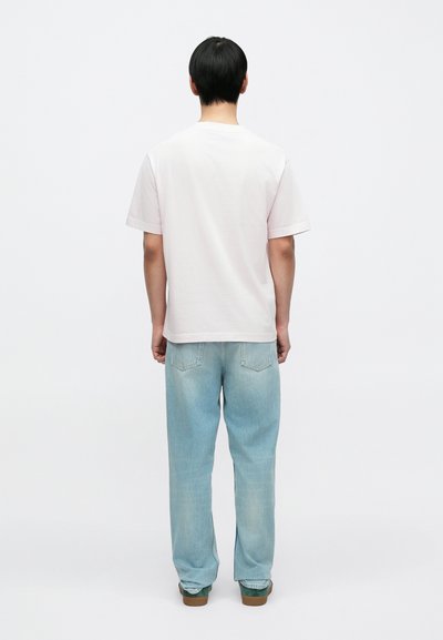 Ανοιχτό ροζ βαμβακερό t-shirt με κοντά μανίκια, συνδυασμένο με ανοιχτό μπλε τζιν παντελόνι και πράσινα παπούτσια. Η στολή φαίνεται από πίσω.