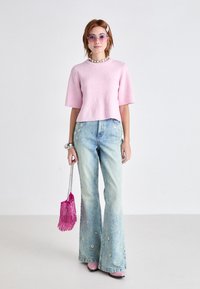 Roze ribbed shirt met korte mouwen, lichtblauwe flared jeans met bloemenborduurwerk, roze hoge hakken en een franje roze handtas.