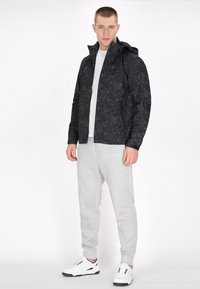 Sort hættetrøje med bladmønster, parret med en hvid crewneck t-shirt og grå sweatpants, afsluttet med hvide sneakers.