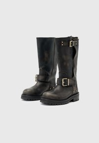 Botas de cuero negro hasta la rodilla con hebillas y herrajes plateados, superficie texturizada y suelas robustas para mayor durabilidad.