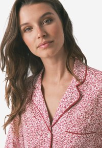 Bluse für Pyjama mit Blumenmuster in Weiß und Rot, mit geknöpftem Kragen, einer Brusttasche und Knopfverschluss. Weicher Stoff.