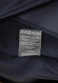 Innenansicht einer marineblauen Fleecejacke mit Pflegeetikett. Weiche Textur, mit Reißverschluss. Das Etikett enthält Waschhinweise und Herkunftsdetails.
