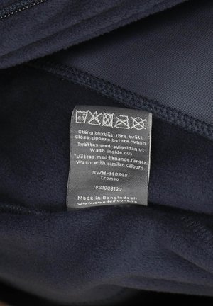 Navy blue fleece jacket interior with care label. Soft texture, featuring a zipper. Label includes washing instructions and origin details.