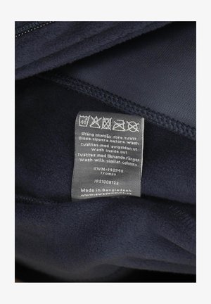 Innenansicht einer marineblauen Fleecejacke mit Pflegeetikett. Weiche Textur, mit Reißverschluss. Das Etikett enthält Waschhinweise und Herkunftsdetails.