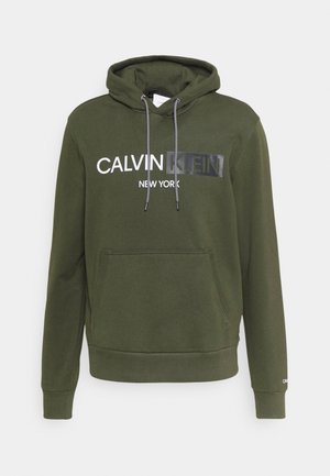 Oliwkowa bluza z kapturem z kieszenią z przodu, czarno-białymi sznurkami i logo „Calvin Klein New York” na piersi.