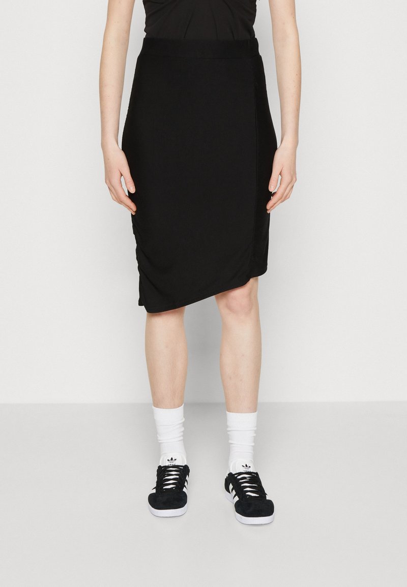 Schwarzer Jersey-Rock mit drapiertem Design, knielang, kombiniert mit weißen Socken und schwarzen Sneakern mit drei Streifen.