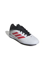 Vit och svart fotbollssko med röda ränder, svarta snören och en låg profil, visad mot vit bakgrund.