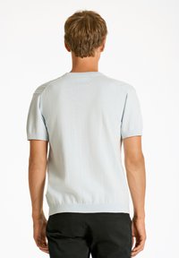 Ljusblå kortärmad tröja med en strukturerad axeldesign och ribbad nederkant, gjord av mjukt, stretchigt material. Bakåtvyn visas.