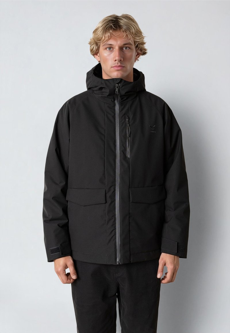 Svart vattentät jacka med dragkedja fram, justerbar huva och två lappar fickor. Har en texturerad tyg och kardborrestängning vid handlederna.