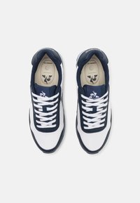 Scarpe sportive bianche e blu navy con tomaia in tessuto, chiusura con lacci, colletto imbottito e accenti blu navy a contrasto lungo la suola.