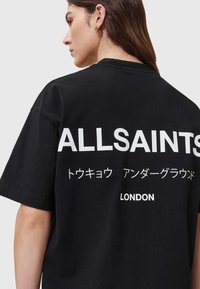 Čierne bavlnené tričko s voľným strihom, na zadnej strane so veľkým bielym textom "ALLSAINTS" a ďalšími znakmi a "LONDON."