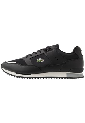 Baskets de sport noires avec un upper en cuir et en mesh, arborant un logo vert, un design à lacets et une semelle en caoutchouc texturé avec des bords dentelés.