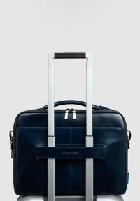 Borsa per laptop in pelle blu scuro attaccata a un carrello argentato con doppia cerniera, manico superiore e cinturino posteriore per un trasporto sicuro.