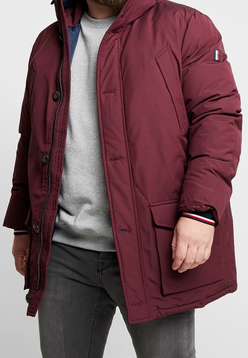 Giacca a vento color bordeaux con chiusura frontale a zip, grandi bottoni e tasche applicate. Polsini a costine con bordatura a contrasto. Interno foderato.