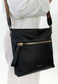 Borsa a tracolla in pelle nera con superficie texturizzata, cerniera dorata e tracolla con motivo. Presenta una tasca frontale e tracolla regolabile.