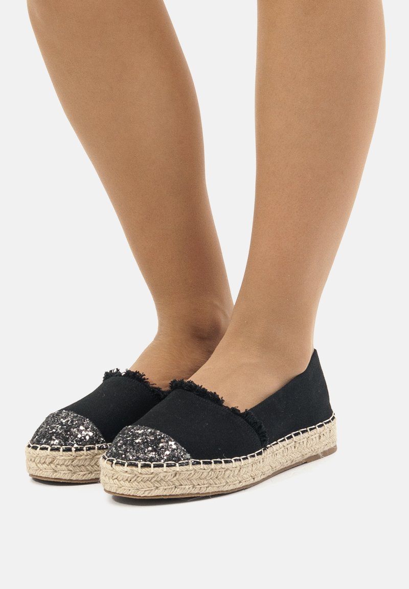 Espadrillas nere con tomaia in tessuto testurizzato, bordi scuciti e una punta nera luccicante. La suola avvolta in juta aggiunge un tocco naturale.