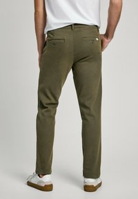 Pantalones de algodón en mezcla de color verde oliva con un corte ajustado, que cuentan con bolsillos traseros con botones y una cinturilla. Usados con zapatillas blancas.