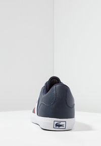 Navy leather sneaker with white rubber sole, featuring red and white accents, smooth texture, branded logo on heel, and padded collar.