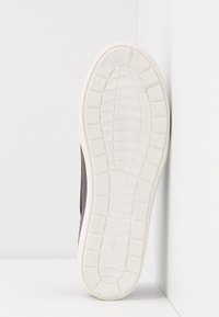 Black sneaker with a rubber white sole, featuring a textured tread pattern. The upper design is smooth and wraps around the foot.