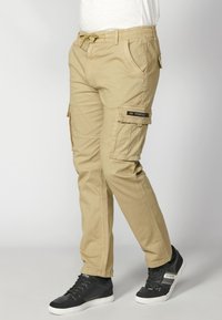 Khaki cargo nohavice s elastickým pásom, viacerými bočnými vreckami a zúženým strihom. Vyrobené z odolnej látky, s hladkou textúrou.