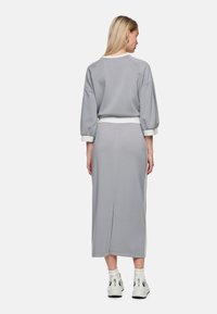 Grauer Pullover mit langen Ärmeln und elastischen Bündchen, kombiniert mit einem passenden grauen Rock mit hinten einem Schlitz. Beide Teile haben eine weiche Textur.