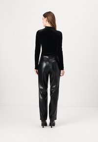 Haut en velours noir à manches longues associé à un pantalon en faux cuir noir taille haute. Le pantalon présente une coupe droite et des poches arrière.