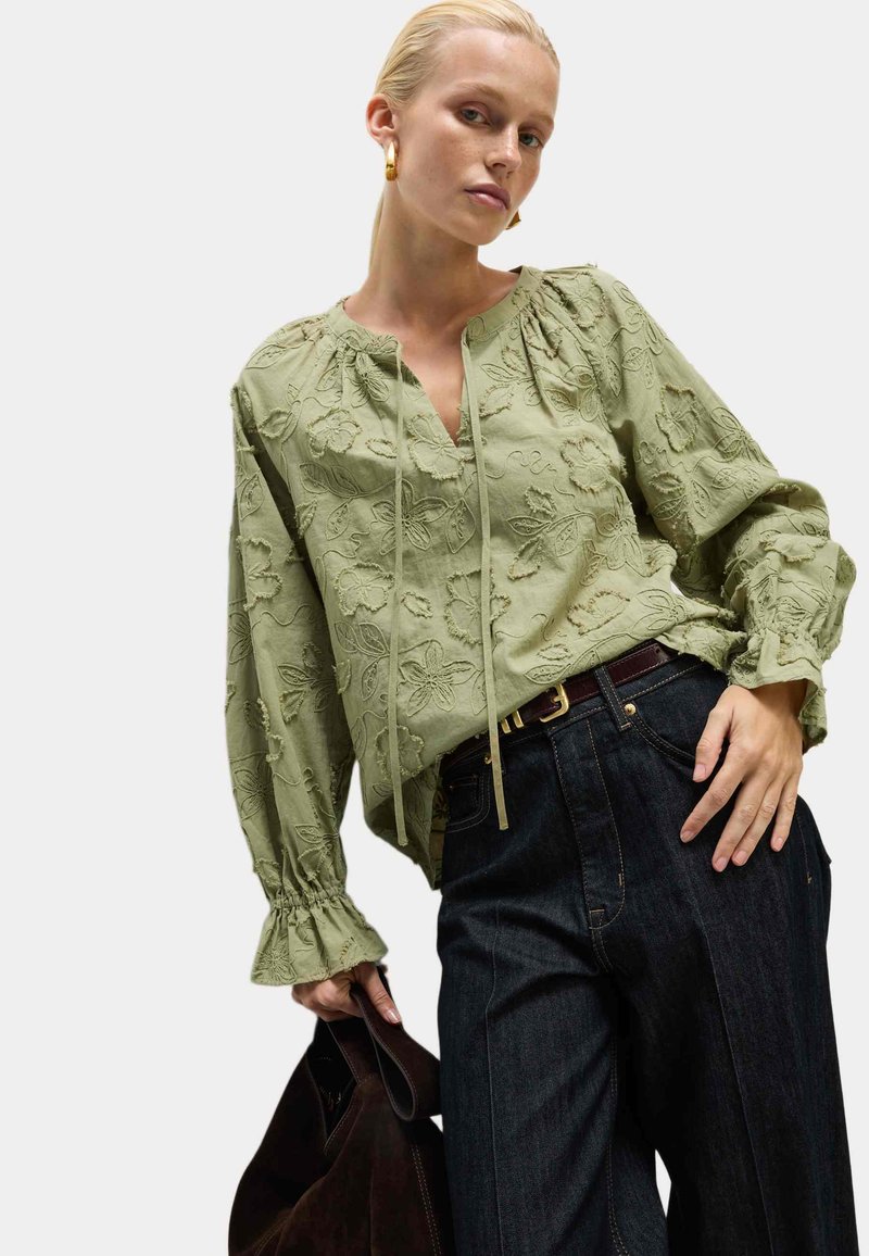 Groen geborduurd blouse met een spleet-halslijn, gathered mouwen en gerimpelde manchetten, gecombineerd met donkerdenim high-waisted broek.