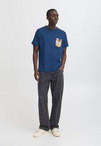 Marineblå bomulds T-shirt med en mønstret lomme, parret med mørkegrå jeans og hvide sneakers med tre striber.