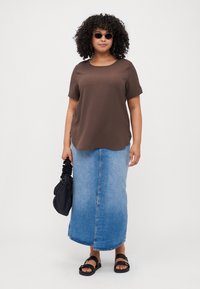 Brown short-sleeve top, faded blue denim maxi skirt, black sandals, and a black bag. Smooth texture, relaxed fit, and slight curve at hem.
