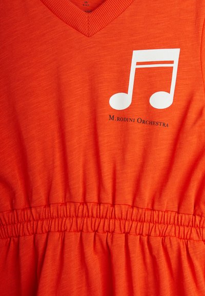 Oranž värviga lühike kleit V-kaelusega, millel on valge muusikanoodi graafika ja tekst "M. rodini Orchestra". Kogutud vöökoht, et luua kuju.
