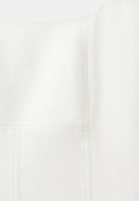 Gros plan d'un tissu blanc avec des lignes de couture verticales et horizontales visibles formant des motifs rectangulaires.